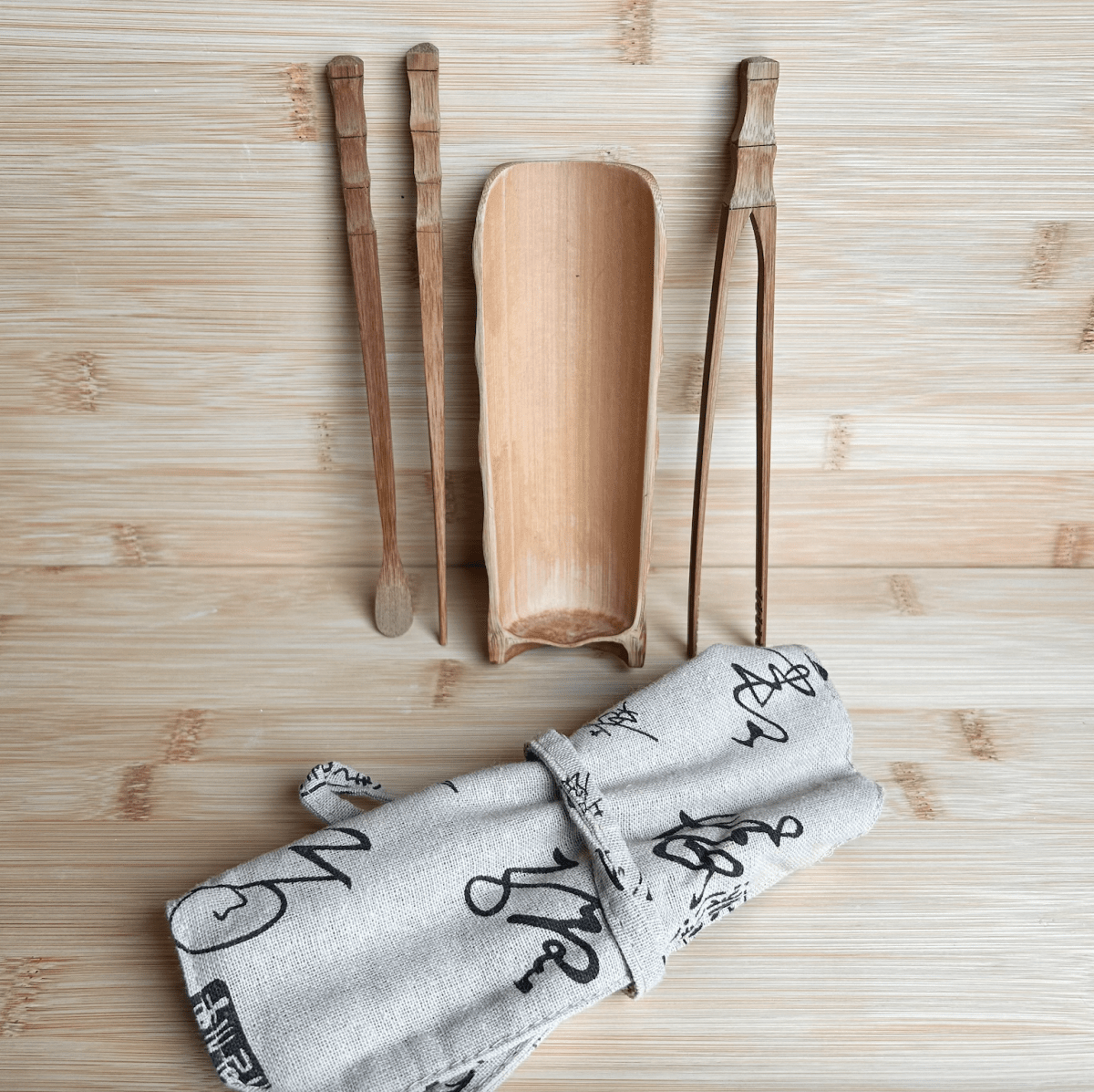 Bamboo Loose Tea Tool Set - marginnotesWooden tea tools including a scoop, two spoons, and a cloth with black text on a wooden surface.
